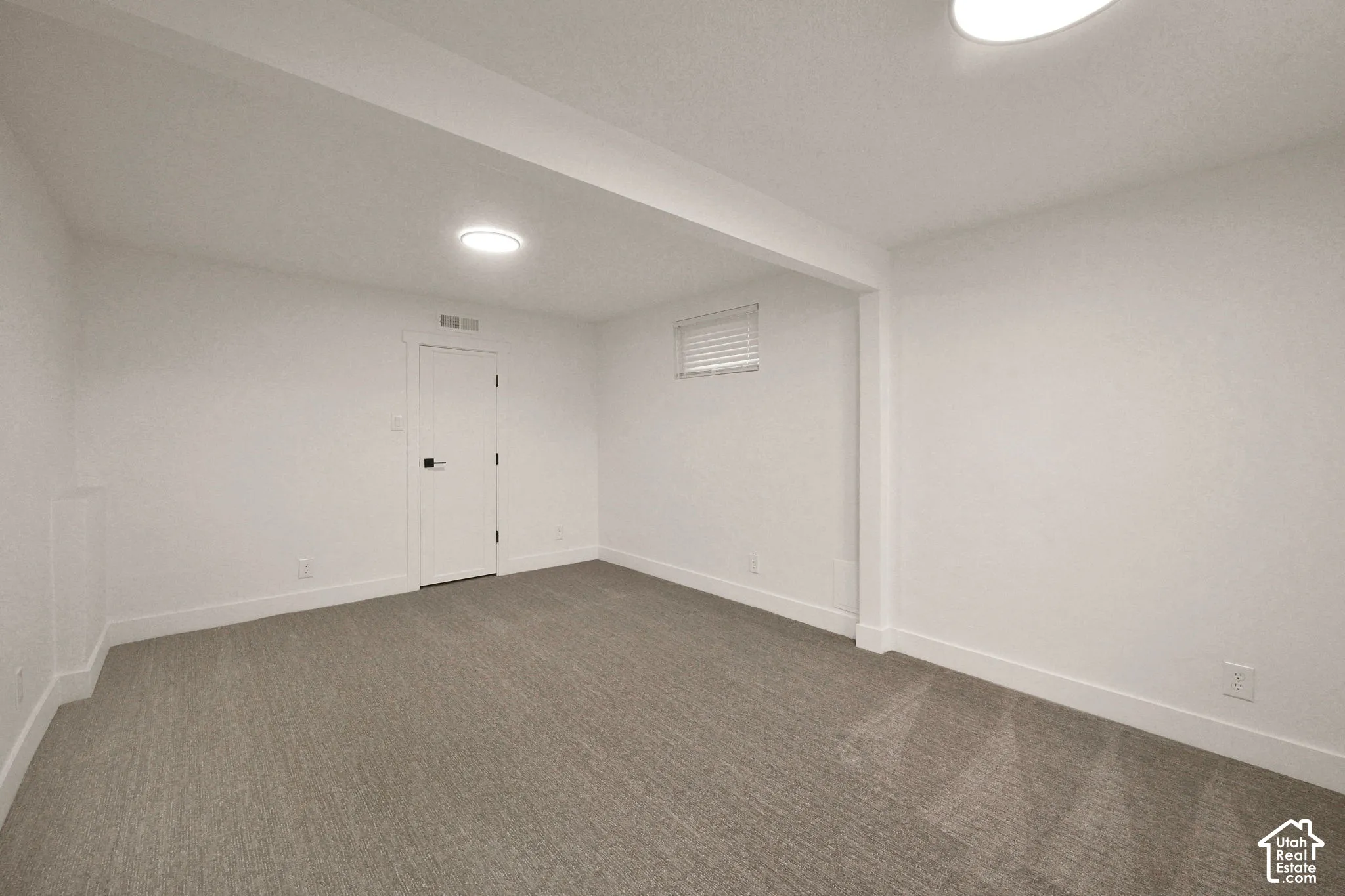 Interior room featuring neutral wall-to-wall carpeting, white walls, two flush-mount ceiling lights, and a single interior door with matte black hardware