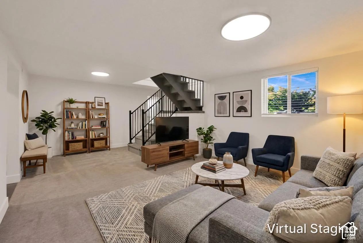 Open-concept room featuring neutral wall-to-wall carpeting, recessed ceiling lighting, a staircase with black metal railings, and a window with horizontal blinds
