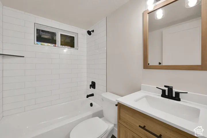 Bathroom featuring white subway tile tub surround, wood-finish vanity with a white countertop, matte black fixtures, and a wood-framed mirror