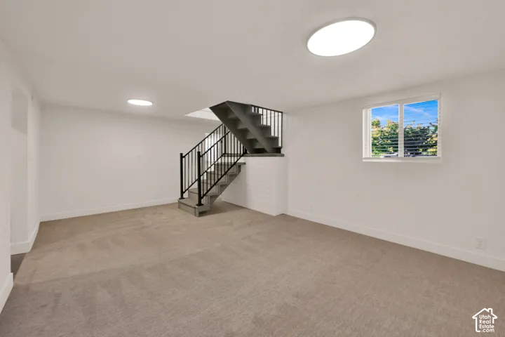 Neutral-toned carpeting, flush-mount circular lighting, and stairs featuring black metal balusters and handrails