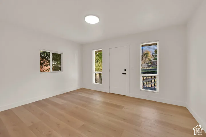 Interior space featuring wood-finish flooring, white walls, flush-mount ceiling lighting, and multiple windows with horizontal blinds