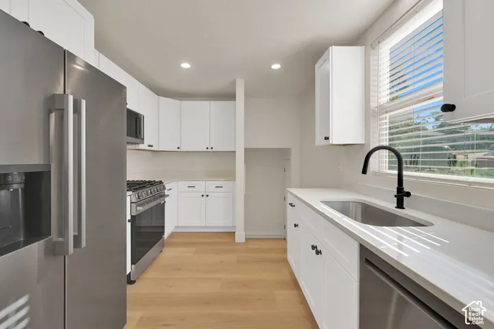 Kitchen featuring white shaker-style cabinetry, stainless steel appliances, quartz countertops, wood-finish flooring, and a matte black gooseneck faucet