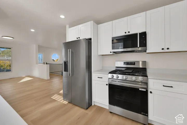 Kitchen featuring white shaker-style cabinetry, stainless steel gas range, stainless steel refrigerator, recessed lighting, and wood-finish flooring