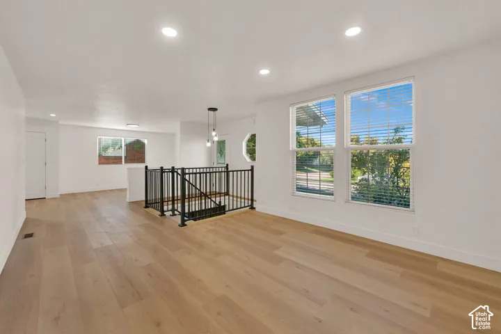 Open-concept interior featuring light wood-finish flooring, recessed lighting, double-pane windows, and a black metal staircase railing