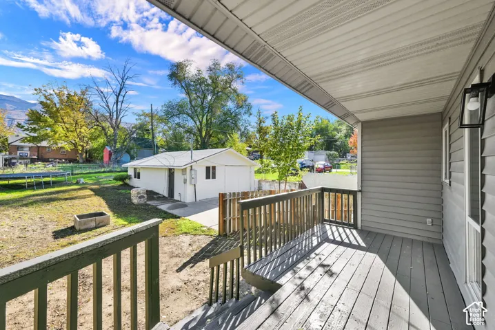 Covered porch with wood-finish decking and railing, detached garage, and fenced backyard area