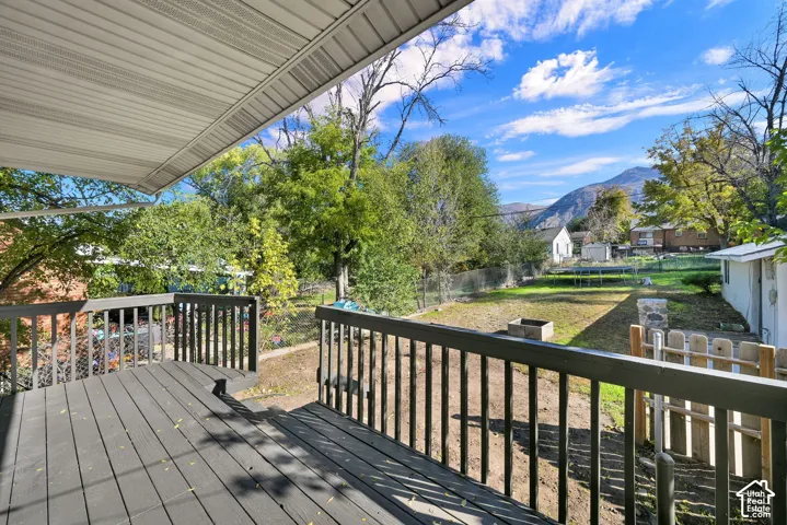 Covered outdoor deck with dark-finish decking and rail perimeter, featuring a backyard, chain-link fencing, and a mountain backdrop