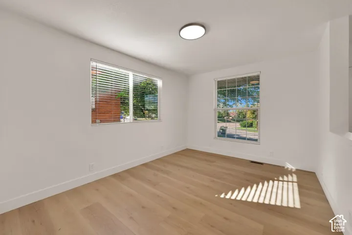 Interior space featuring wood-finish flooring, dual windows with fitted blinds, and a neutral white paint palette complemented by a flush-mount circular LED light fixture