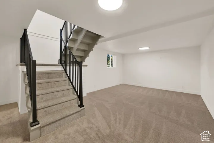 Open interior space featuring neutral carpeting, a staircase with matte black metal railings, and dual flush-mount ceiling lighting
