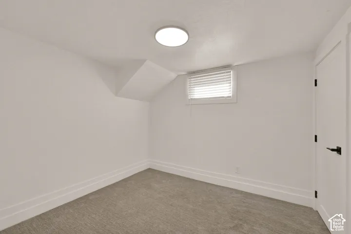 Interior space featuring neutral-toned carpeting, recessed ceiling lighting, a single horizontal window with fitted blinds, and a paneled door with matte black hardware