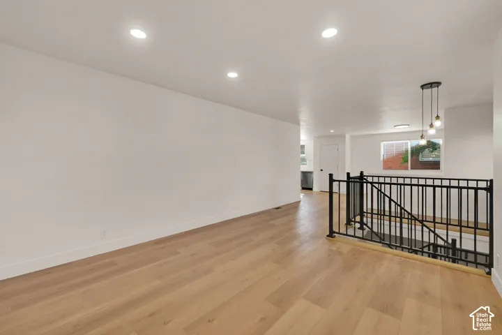 Open floor plan featuring wood-finish flooring, recessed lighting, matte black iron stair railing, and a multi-pendant light fixture