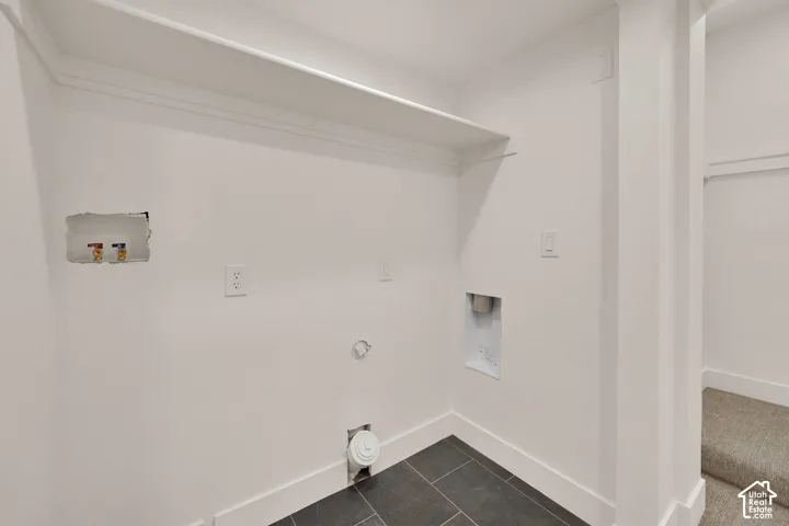 Laundry alcove featuring dark tile flooring, a built-in wall shelf, and dedicated water and electrical hookups