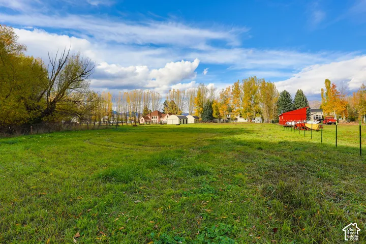 Expansive grounds featuring a vast open lawn, perimeter fencing, mature trees, and a detached red outbuilding