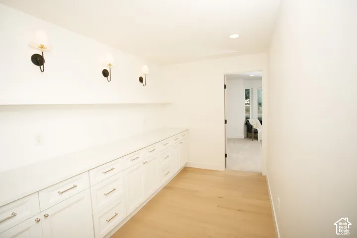 Built-in white cabinetry with stone countertops, integrated wall sconces, wood-finish flooring, and a floating shelving unit