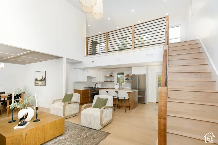 Open-concept interior featuring double-height ceilings, wood-finish flooring, a staircase with horizontal metal railing, and recessed lighting
