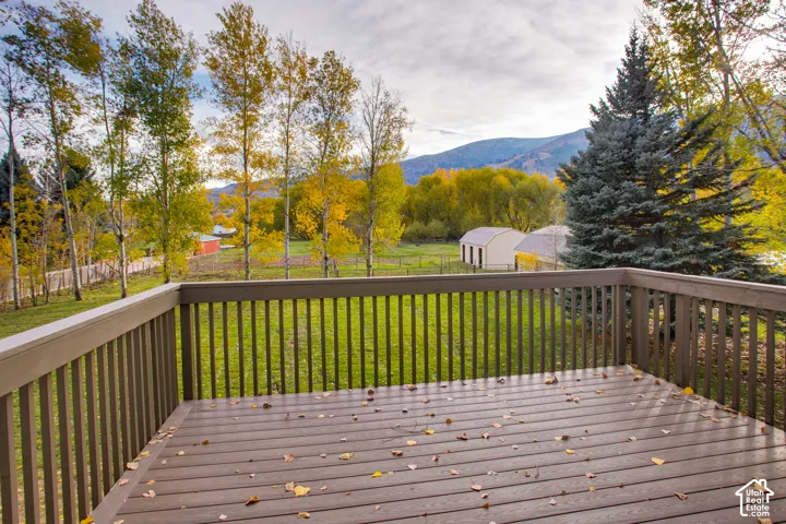 Elevated wood deck featuring vertical spindle railings, overlooking a grassy yard with mature trees and mountain scenery