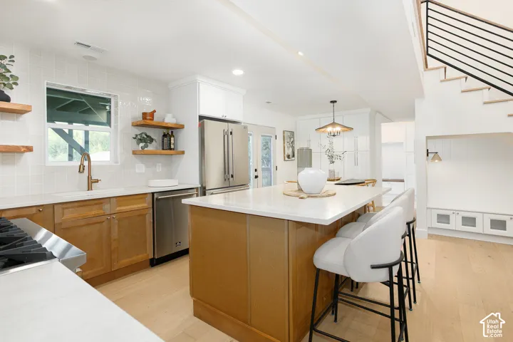 Kitchen featuring a central island with a solid surface countertop, wood cabinetry, floating wood shelving, stainless steel appliances, and wood-finish flooring
