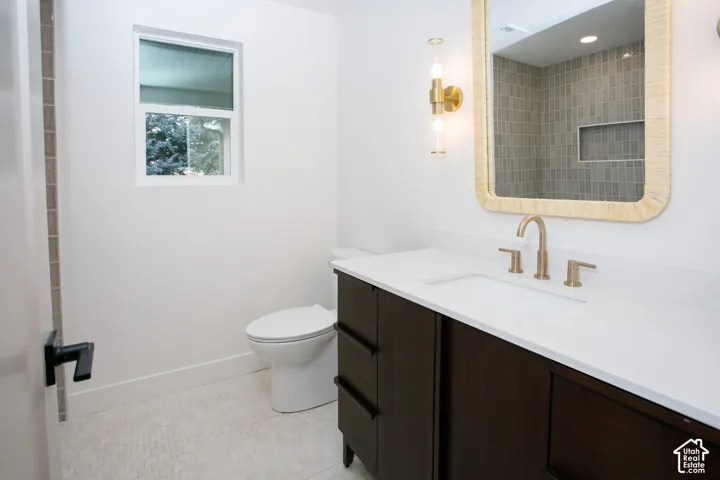 Dark wood-finish vanity with a white countertop and gold-toned faucet, complemented by dual-light gold-toned wall sconces, a textured-frame mirror, and tiled shower surround with an integrated recessed niche