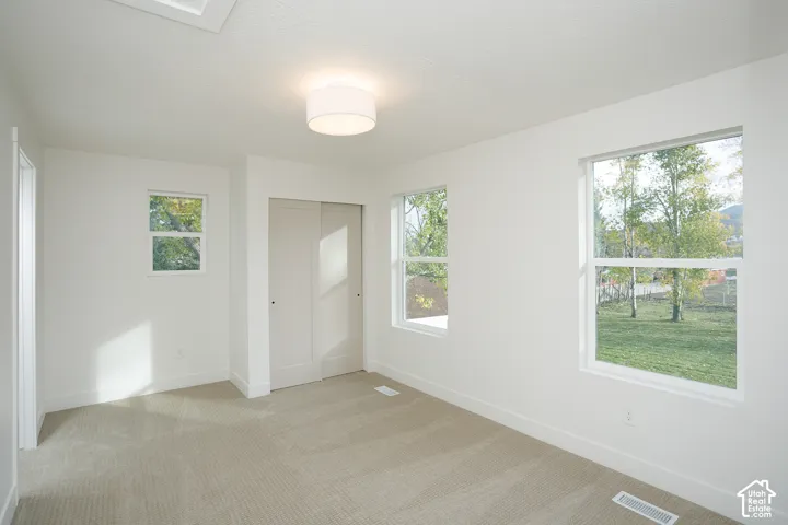 Neutral-toned carpeting, triple-window configuration, dual-panel sliding closet doors, and flush-mount drum lighting
