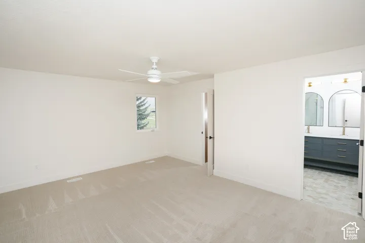 Neutral-toned wall-to-wall carpeting, ceiling-mounted paddle fan with integrated lighting, and white interior walls
