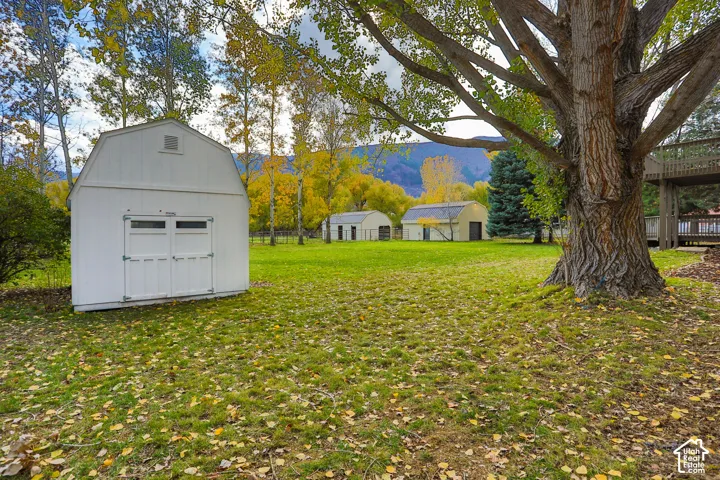 Expansive grounds featuring a white gambrel-style storage shed, additional outbuildings, mature trees, and mountain backdrop