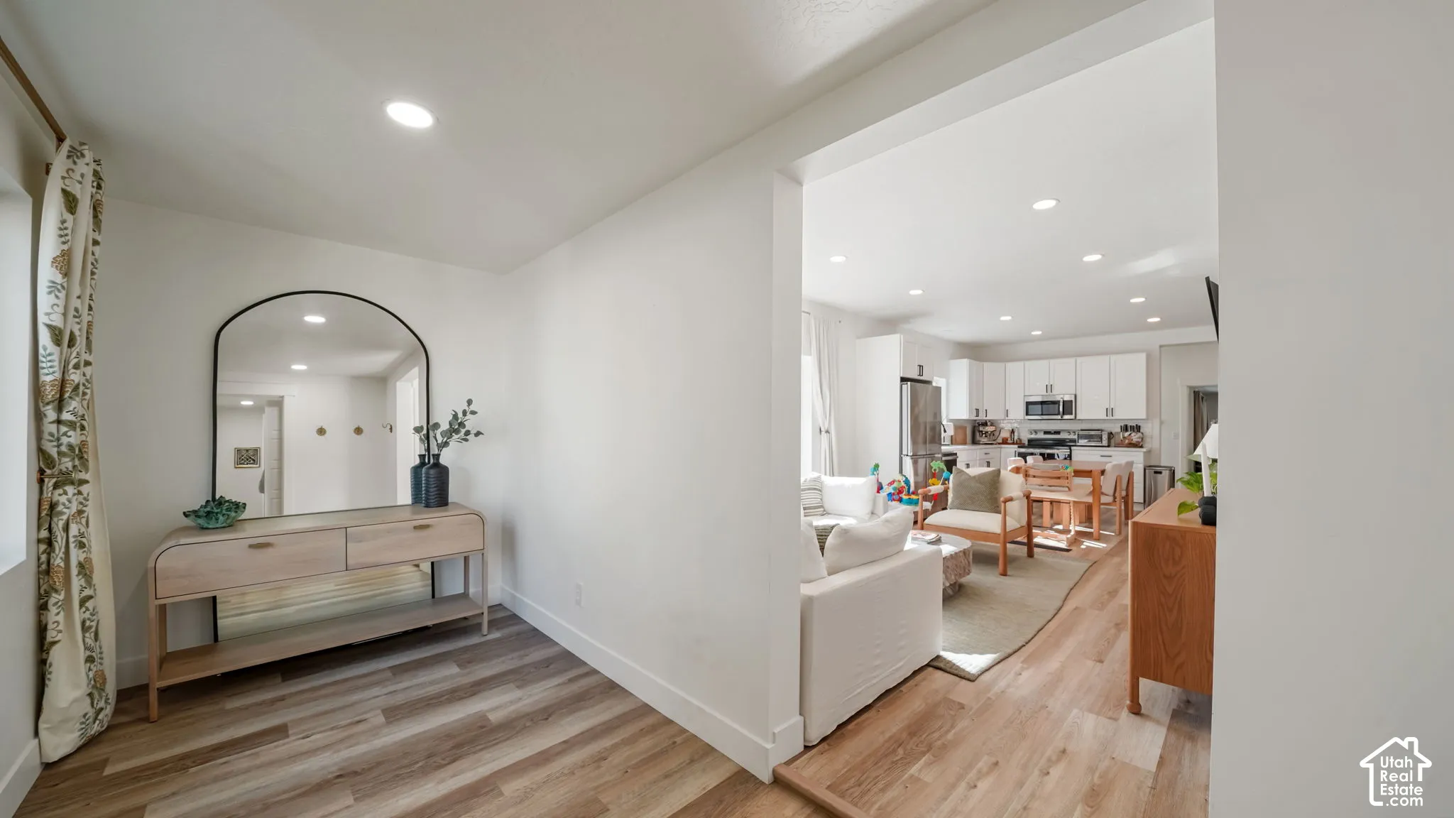 Wood-finish flooring, recessed lighting, and kitchen featuring white cabinetry and stainless steel appliances