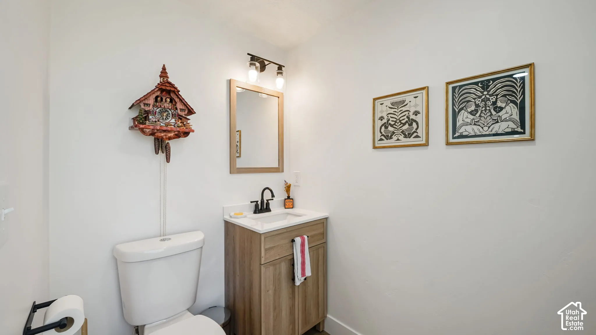 Wood-finish vanity cabinet, white rectangular countertop sink, matte black gooseneck faucet, light-toned framed mirror, and two-light wall fixture