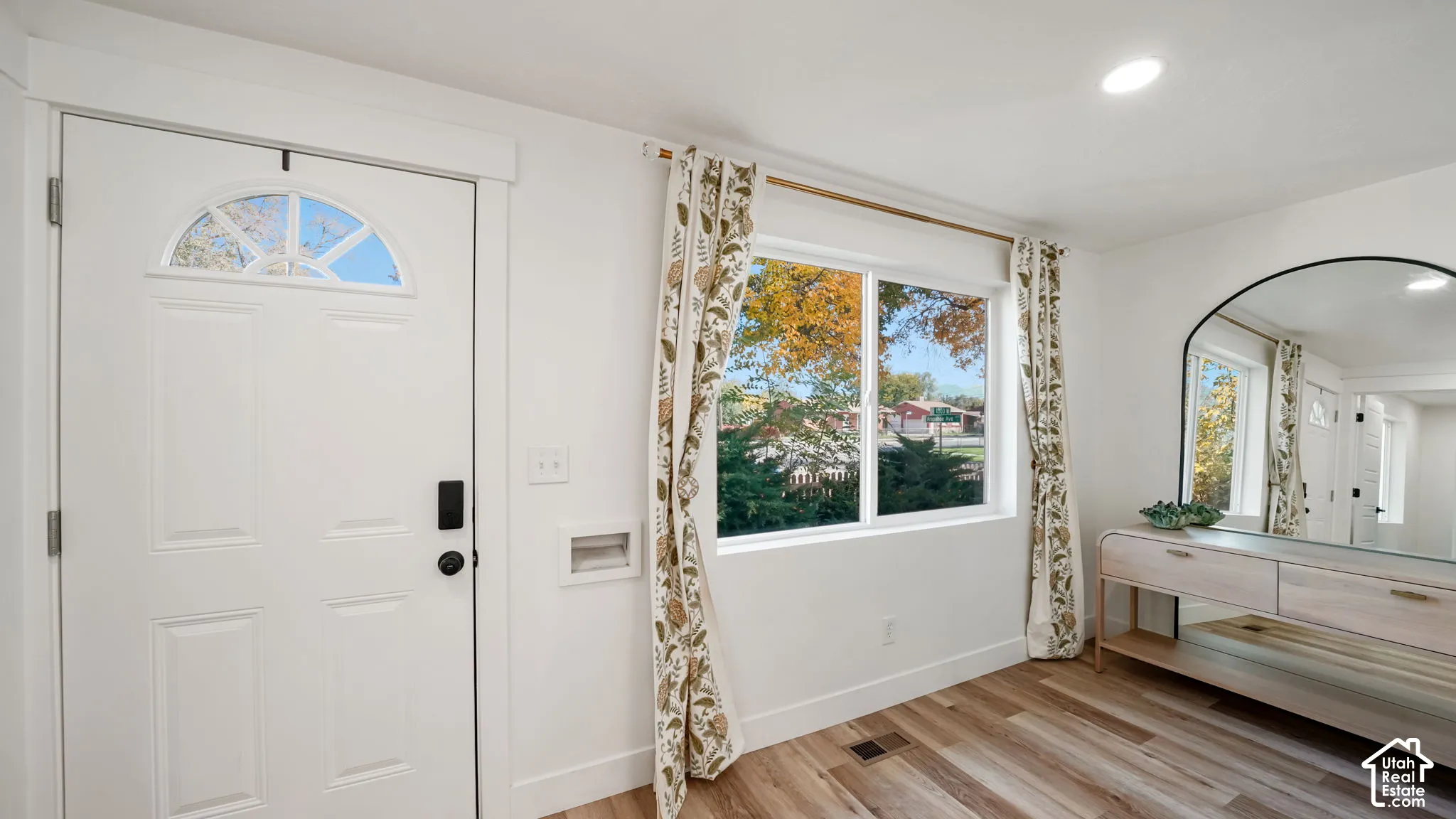 White exterior entry door with arched window insert, large picture window, and wood-finish flooring