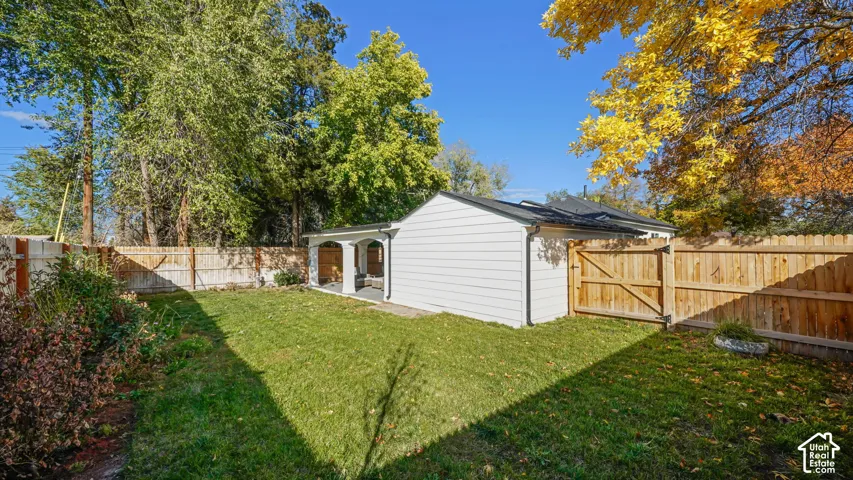 Enclosed backyard featuring a manicured lawn, full-height wood privacy fencing, a covered patio with arched architectural detailing, and mature trees