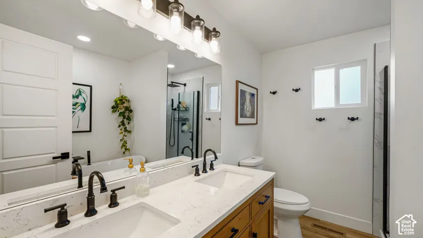 Double vanity with stone-finish countertops, undermount sinks, matte black widespread faucets, wood-finish cabinetry, and a full-width vanity mirror with integrated multi-bulb lighting