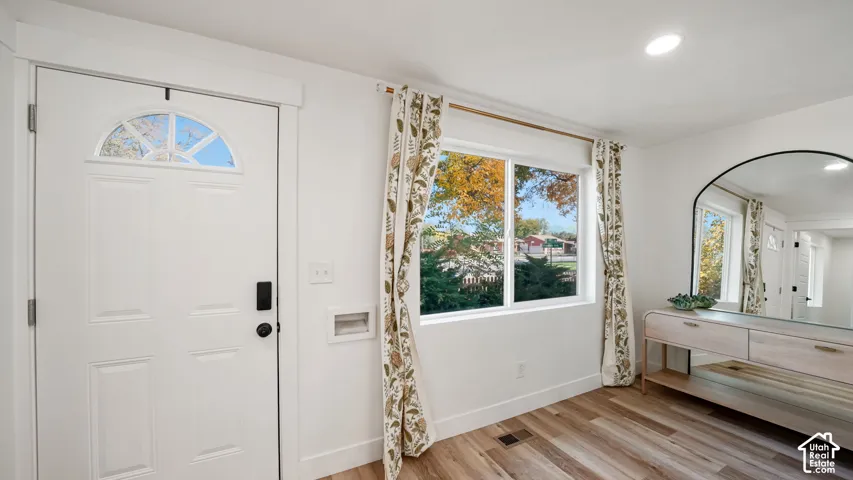 White exterior entry door with arched window insert, large picture window, and wood-finish flooring