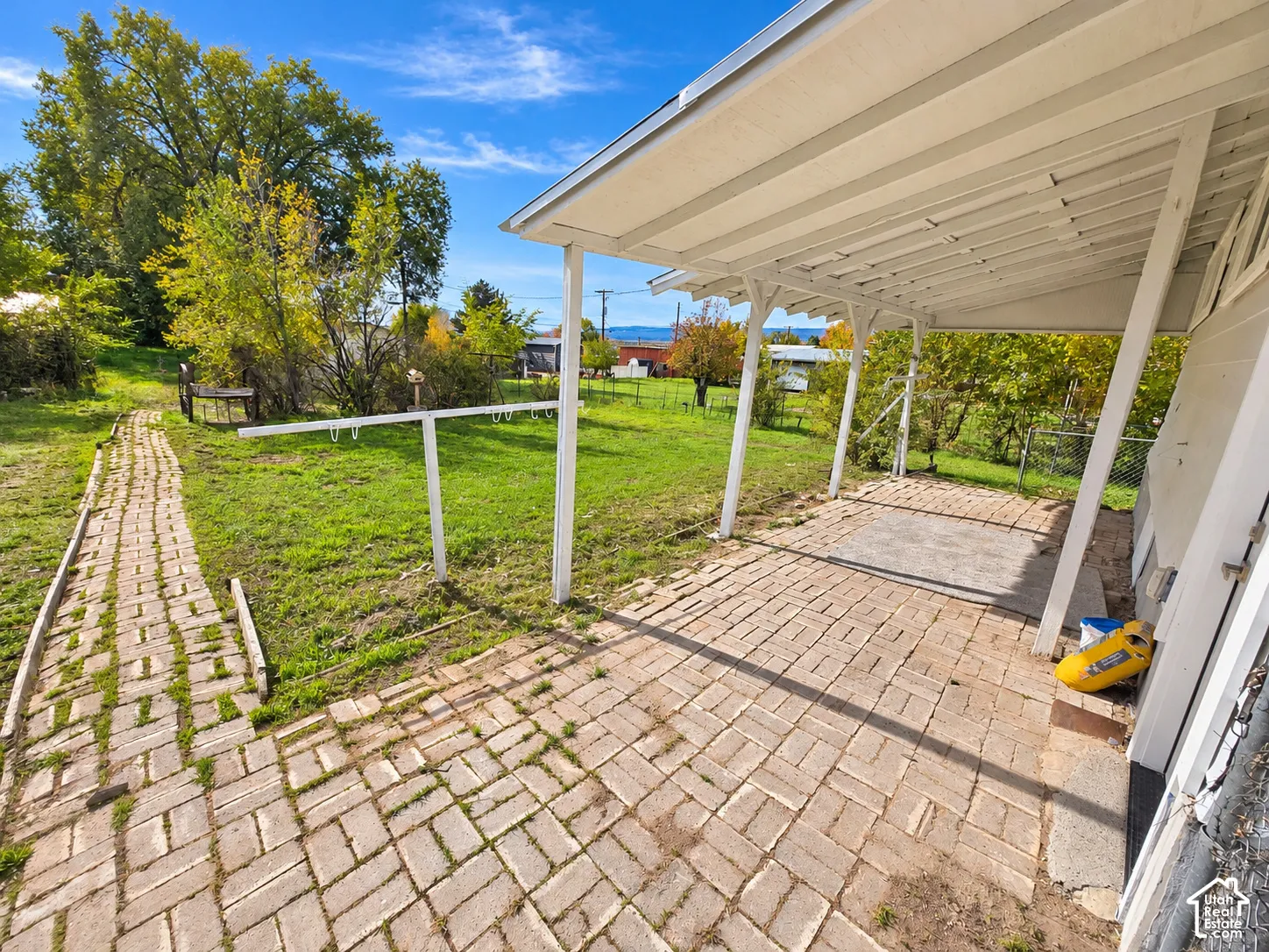 Covered patio with brick flooring, concrete masonry unit walkway, and expansive rear yard