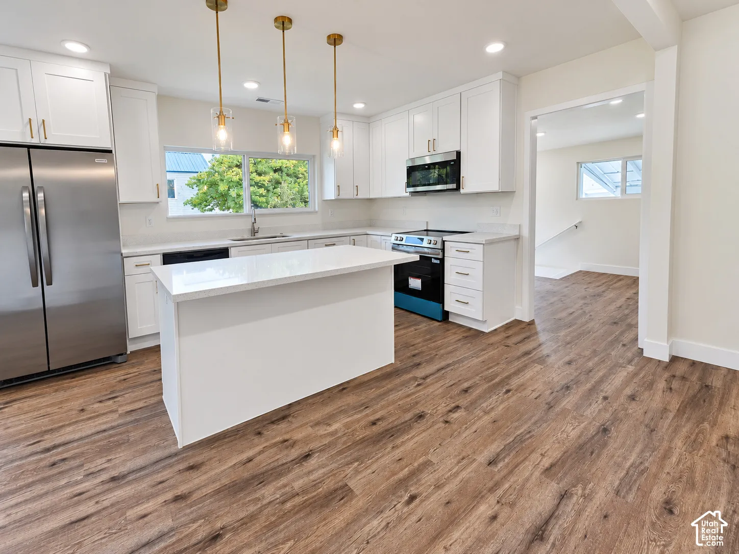Kitchen featuring white cabinetry, quartz countertops, wood-finish flooring, stainless steel appliances, and brass-tone pendant lighting