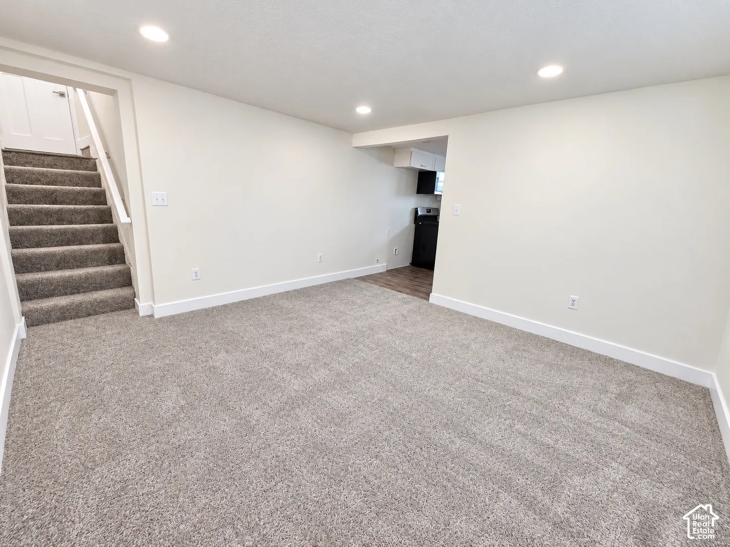 Neutral-toned carpeting, recessed ceiling lighting, staircase with carpeted treads, and wood-finish flooring in the secondary area