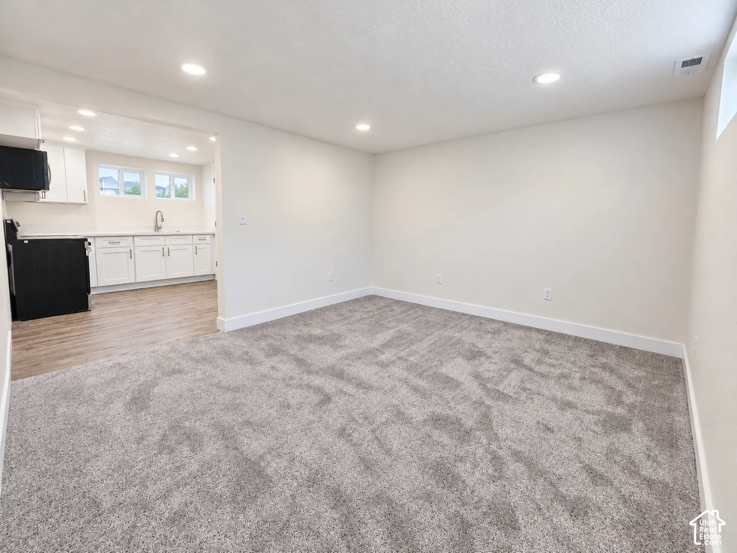Neutral-toned carpeting, recessed lighting, and white cabinetry featuring a stainless steel faucet and wood-finish flooring