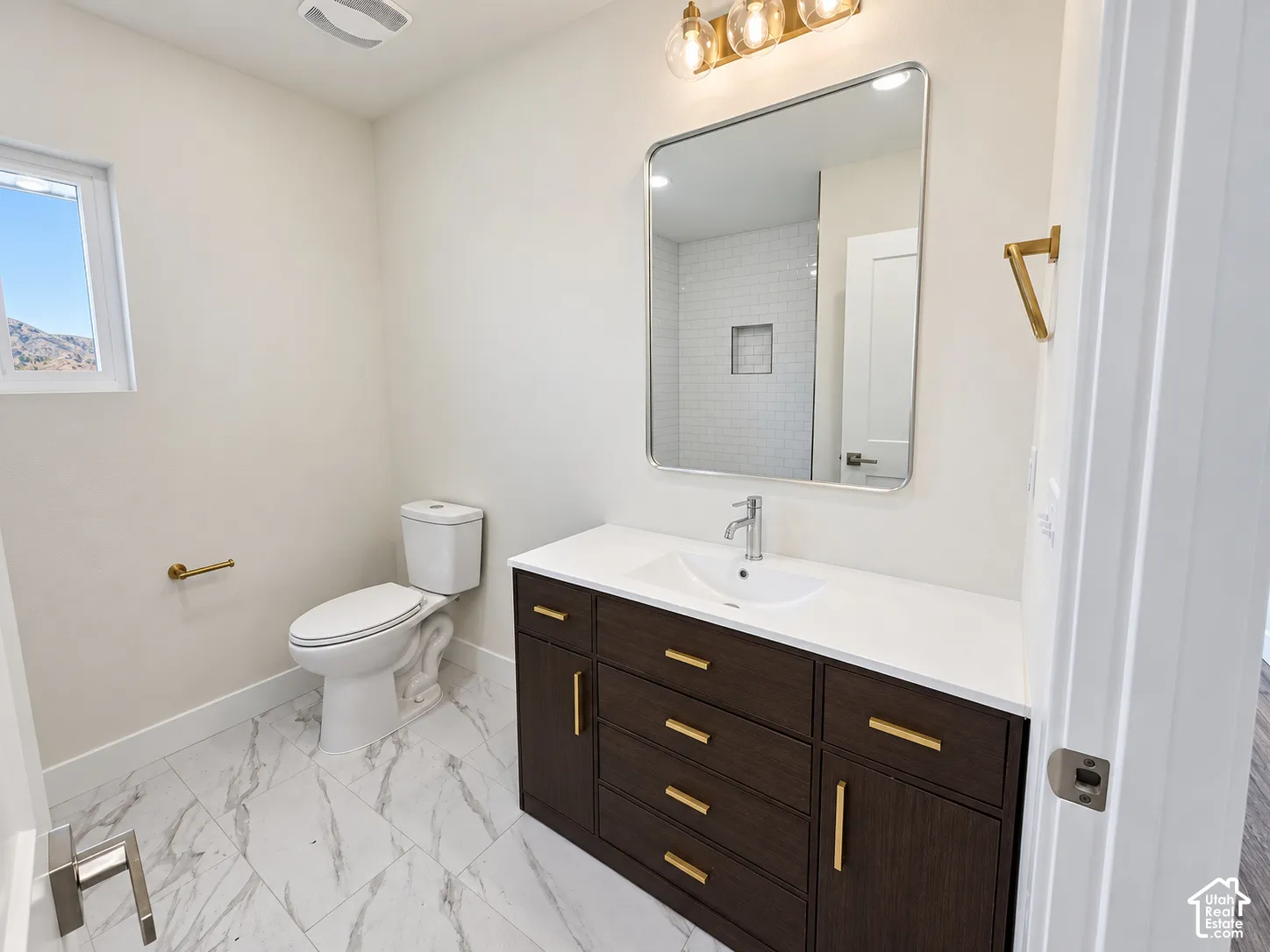Bathroom featuring dark wood-finish vanity with white countertop, rectangular vessel-style sink, gold-tone hardware, and large-format tile flooring