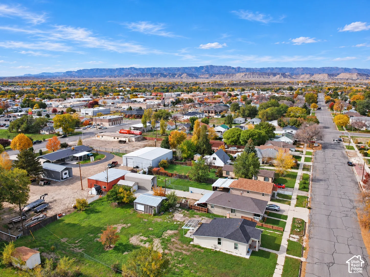 Aerial perspective of the residential property featuring a detached garage, a storage outbuilding, mature landscaping, and prominent mountain backdrops