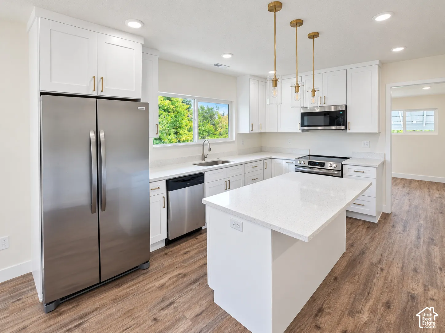 Kitchen featuring white shaker-style cabinetry, quartz countertops, stainless steel appliances, a central island, and wood-finish flooring