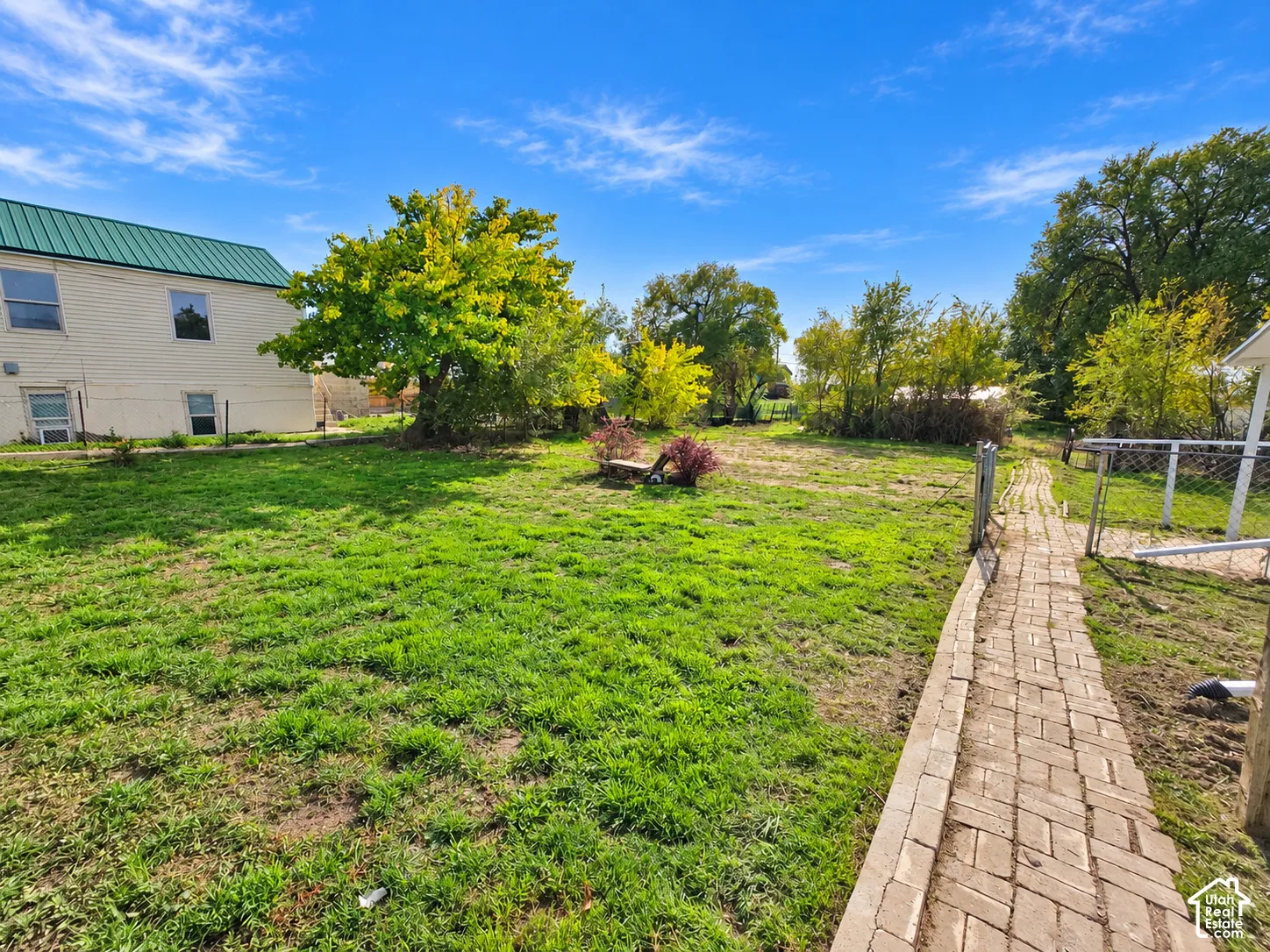Expansive lawn featuring mature trees, a brick-paver pathway, and perimeter metal fencing