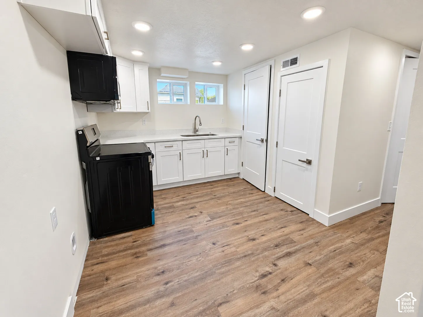 Kitchen area featuring white Shaker-style cabinetry, white countertops, wood-finish flooring, recessed lighting, and a black freestanding range