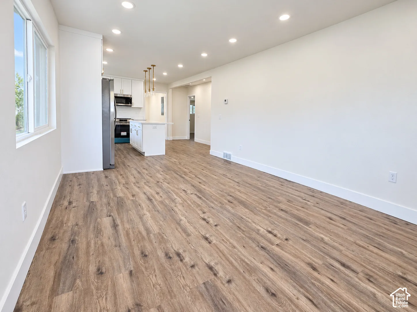 Open-concept interior featuring wood-finish flooring, recessed lighting, white cabinetry, a central kitchen island, and stainless-steel appliances