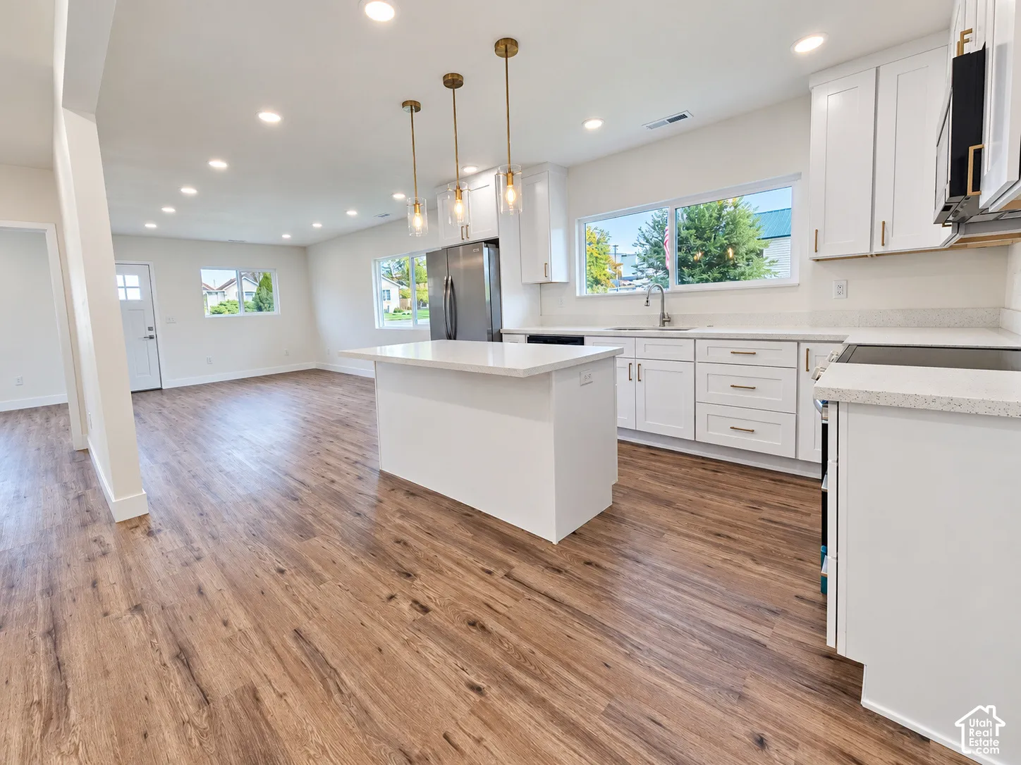 Kitchen featuring white cabinetry, quartz countertops, a central island, wood-finish flooring, and metallic pendant lighting