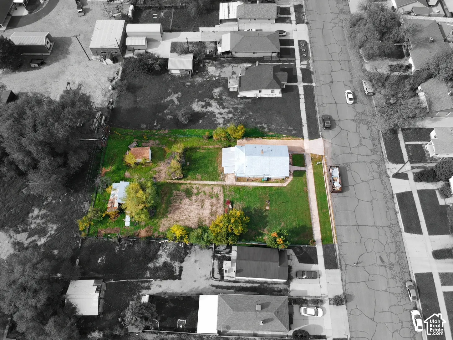Aerial perspective of a corner lot featuring extensive lawn space, mature trees, a detached secondary structure, and paved driveway access