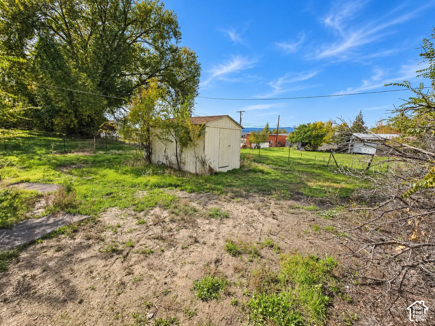 Expansive parcel of land featuring a detached storage structure, mature trees, and perimeter fencing