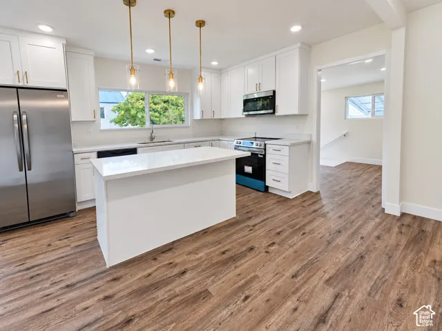 Kitchen featuring white cabinetry, quartz countertops, wood-finish flooring, stainless steel appliances, and brass-tone pendant lighting