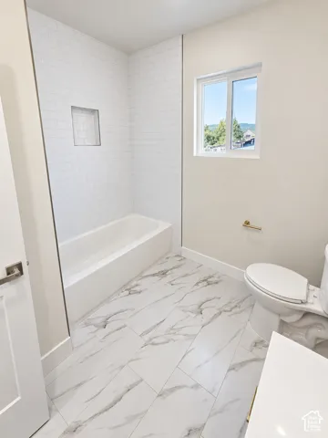 Bathroom featuring large-format tile flooring with a veined pattern, white subway tile tub surround with a recessed niche, and gold-finish hardware