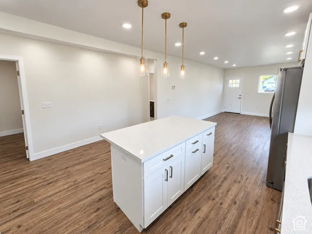 Kitchen island featuring a white base with cabinet storage, topped with a quartz countertop, complemented by three brass-finish pendant lights and wood-finish flooring