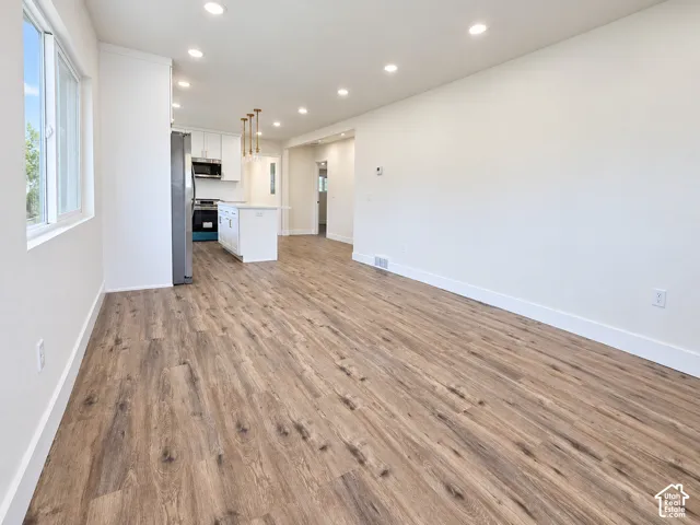 Open-concept interior featuring wood-finish flooring, recessed lighting, white cabinetry, a central kitchen island, and stainless-steel appliances