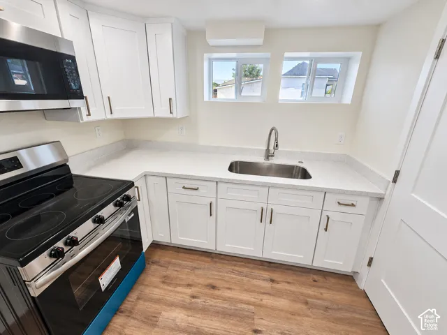 Kitchen featuring white shaker-style cabinetry, solid-surface countertops, a stainless steel undermount sink with a gooseneck faucet, an over-the-range microwave, and wood-finish flooring