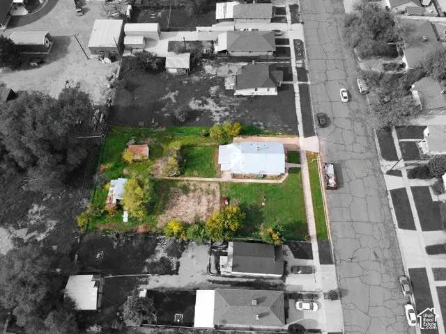 Aerial perspective of a corner lot featuring extensive lawn space, mature trees, a detached secondary structure, and paved driveway access