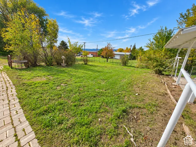 Spacious backyard featuring a brick paver walkway, white metal structural framing, and mature trees